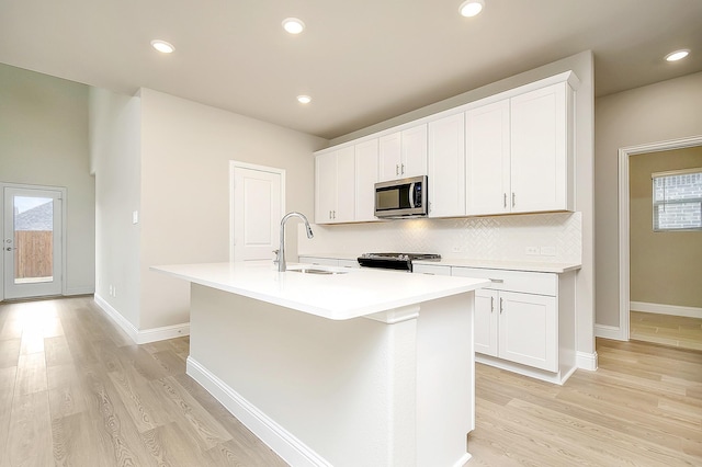 kitchen featuring white cabinetry, sink, stainless steel appliances, and an island with sink