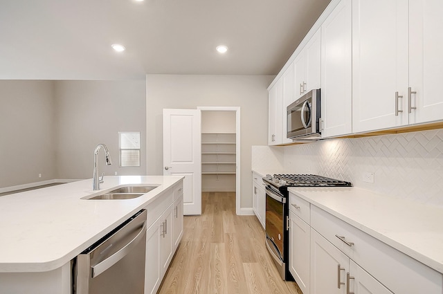 kitchen with sink, light hardwood / wood-style flooring, appliances with stainless steel finishes, a kitchen island with sink, and white cabinetry