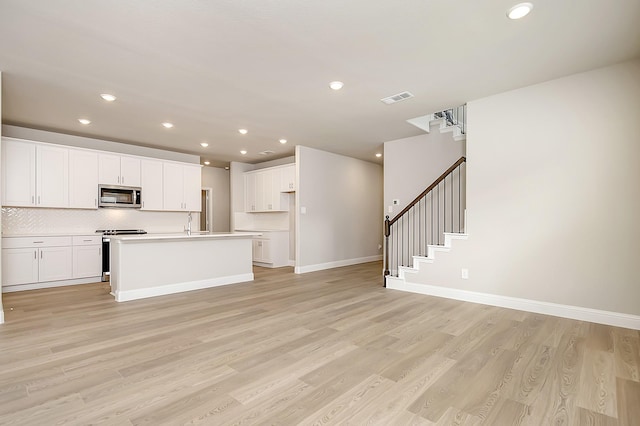 kitchen with white cabinetry, appliances with stainless steel finishes, an island with sink, and light wood-type flooring