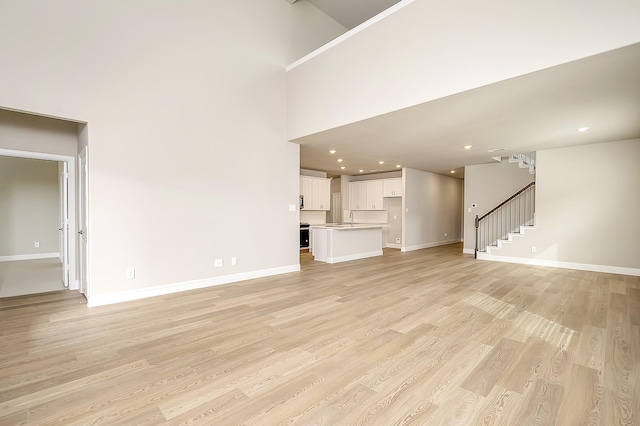 unfurnished living room with sink, light hardwood / wood-style floors, and a high ceiling