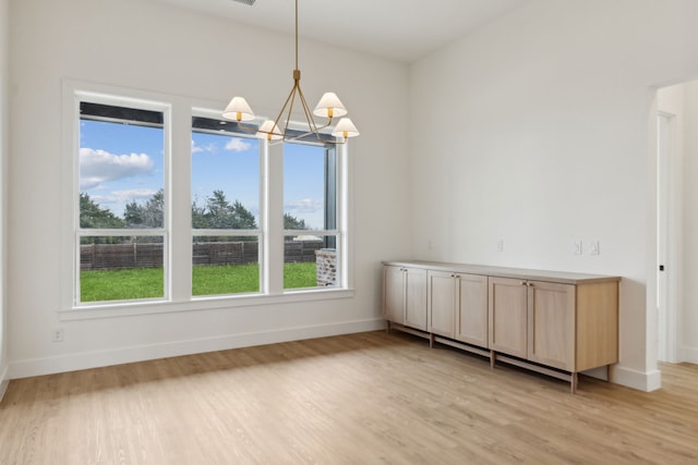 unfurnished dining area with plenty of natural light, an inviting chandelier, and light hardwood / wood-style flooring