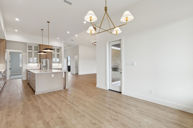 kitchen featuring hanging light fixtures, a center island with sink, stainless steel fridge, and light hardwood / wood-style flooring