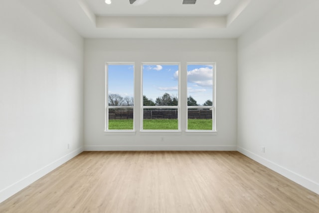 spare room with a tray ceiling, ceiling fan, and light wood-type flooring