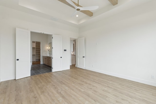 unfurnished bedroom featuring a tray ceiling, ensuite bath, ceiling fan, and light wood-type flooring