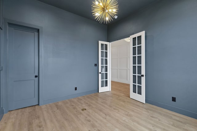 unfurnished room featuring an inviting chandelier, light hardwood / wood-style floors, and french doors