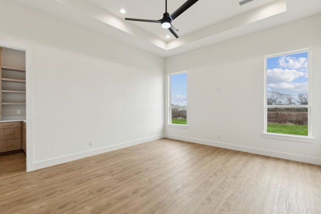 empty room featuring ceiling fan, plenty of natural light, a tray ceiling, and light hardwood / wood-style flooring