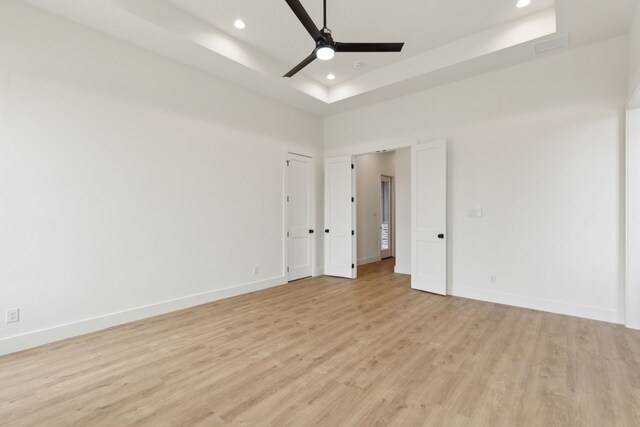 unfurnished room with ceiling fan, a raised ceiling, light hardwood / wood-style floors, and a high ceiling