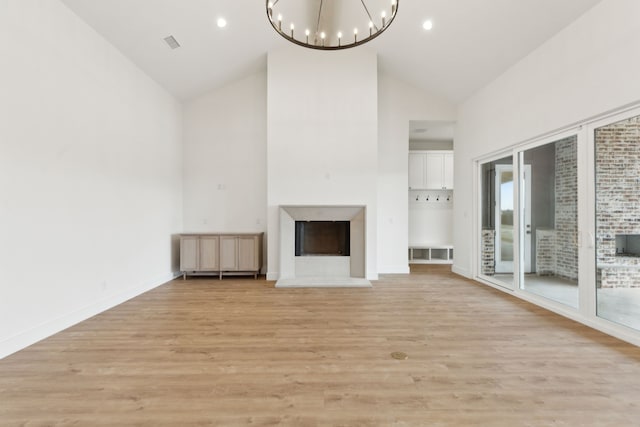 unfurnished living room with light hardwood / wood-style flooring, high vaulted ceiling, and a chandelier