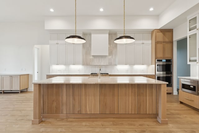 kitchen with white cabinetry, hanging light fixtures, an island with sink, and stainless steel double oven