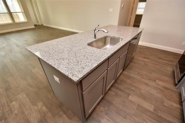 kitchen with light stone counters, dark hardwood / wood-style floors, a kitchen island with sink, and sink