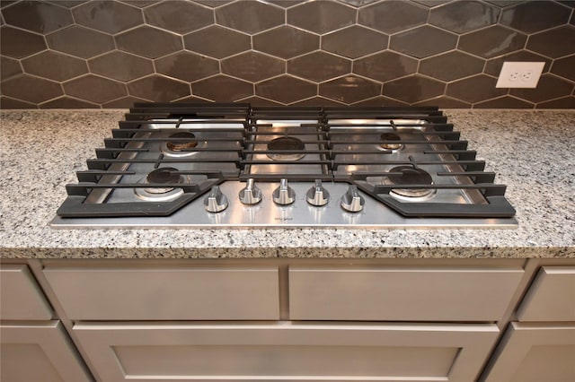 details featuring light stone counters, backsplash, and stainless steel gas stovetop