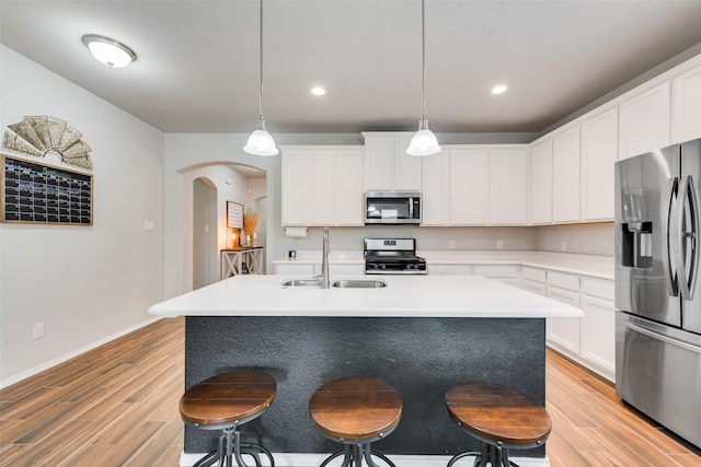 kitchen with light wood-style flooring, stainless steel appliances, arched walkways, a sink, and a breakfast bar area
