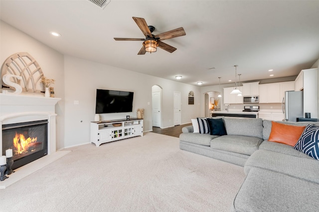 living room featuring a glass covered fireplace, arched walkways, recessed lighting, and a ceiling fan