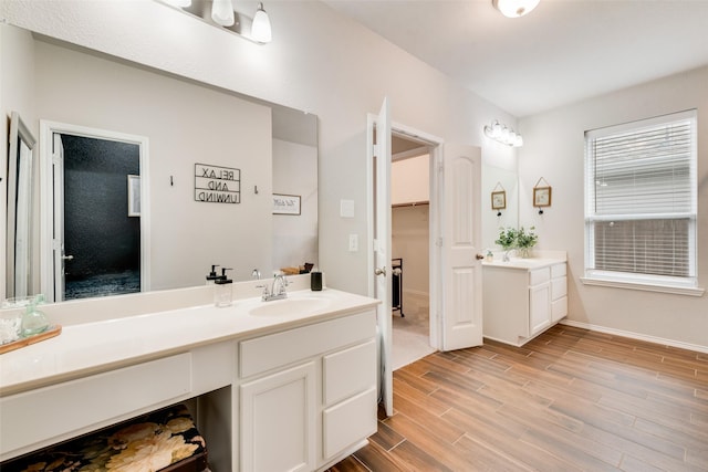 bathroom with a sink, two vanities, wood finished floors, a spacious closet, and baseboards