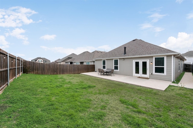 rear view of house featuring a fenced backyard, a lawn, a shingled roof, and a patio