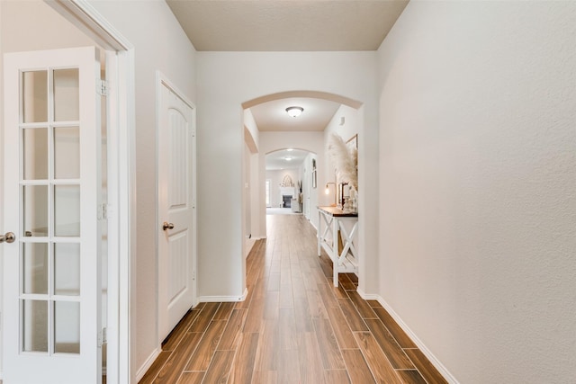 corridor featuring arched walkways, baseboards, and wood tiled floor