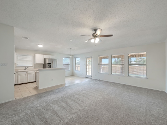 unfurnished living room featuring sink, a textured ceiling, light colored carpet, and ceiling fan