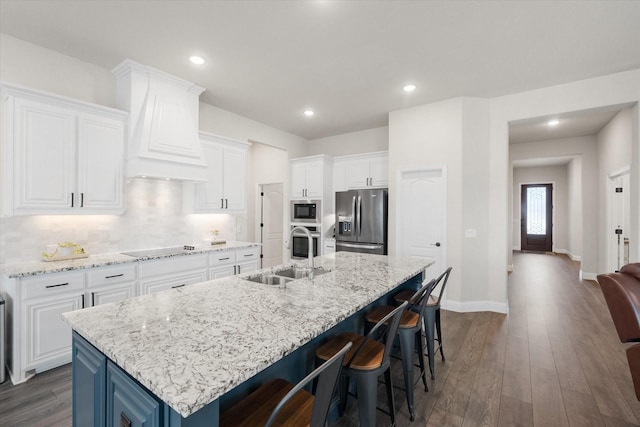 kitchen with sink, a large island with sink, appliances with stainless steel finishes, custom range hood, and white cabinets