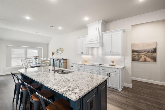 kitchen with sink, premium range hood, an island with sink, white cabinets, and decorative backsplash