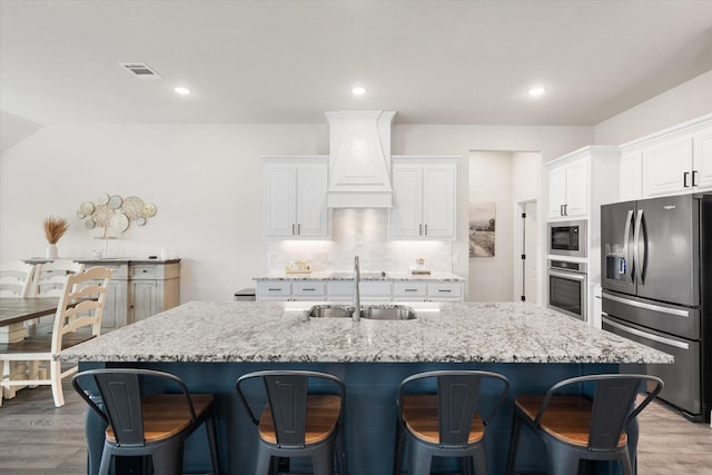 kitchen featuring premium range hood, sink, white cabinetry, an island with sink, and stainless steel appliances