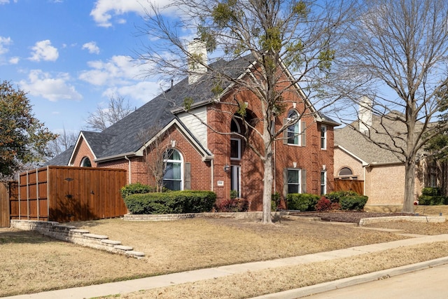 view of front facade with fence, brick siding, roof with shingles, and a chimney