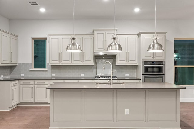 kitchen with decorative light fixtures, light hardwood / wood-style floors, appliances with stainless steel finishes, and a center island with sink