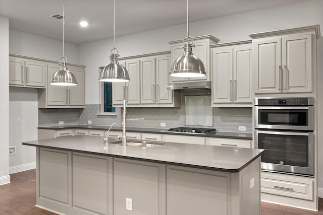 kitchen with dark hardwood / wood-style floors, decorative light fixtures, backsplash, stainless steel appliances, and a center island with sink