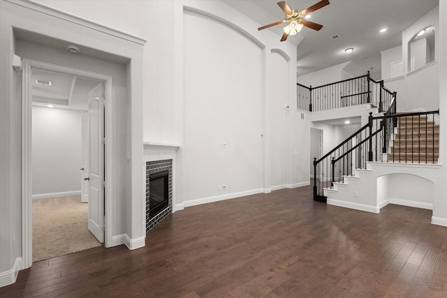 unfurnished living room with a tile fireplace, dark wood-type flooring, ceiling fan, and a towering ceiling