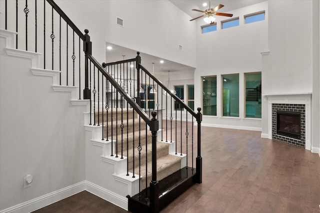 stairs with ceiling fan, hardwood / wood-style floors, and a tile fireplace