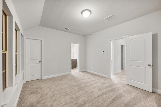 unfurnished bedroom featuring light colored carpet, vaulted ceiling, and ensuite bath