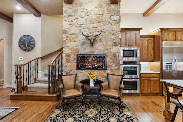 interior space with beam ceiling, a fireplace, light wood finished floors, and stairs