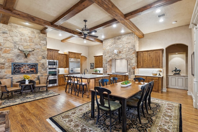 dining room with arched walkways, beam ceiling, light wood finished floors, visible vents, and a ceiling fan