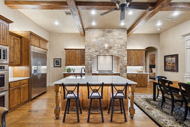 kitchen featuring arched walkways, stainless steel appliances, light wood-type flooring, and beam ceiling