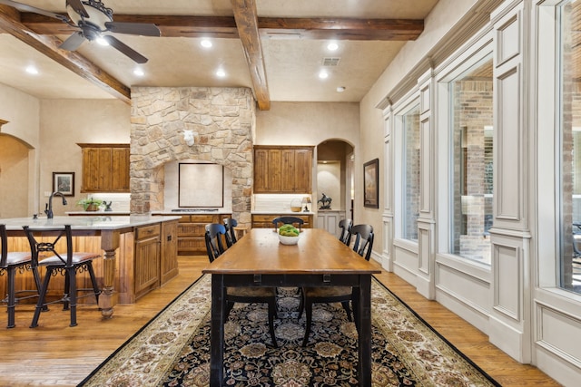 dining space featuring arched walkways, beamed ceiling, light wood-style flooring, and a healthy amount of sunlight