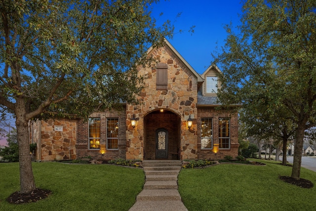 tudor-style house featuring stone siding, brick siding, and a front yard