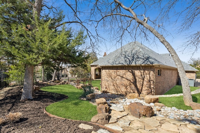 view of property exterior featuring a chimney, fence, a lawn, and brick siding