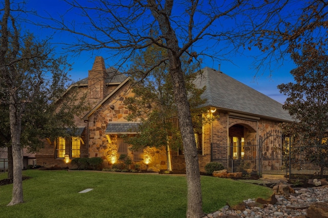 tudor home featuring a shingled roof, stone siding, brick siding, and a yard