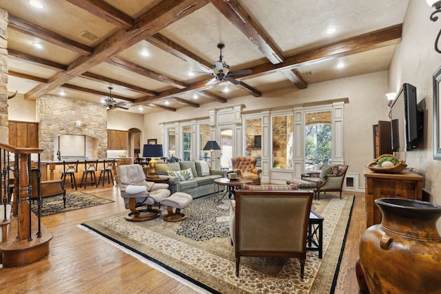 living room with ceiling fan, arched walkways, coffered ceiling, wood finished floors, and beam ceiling