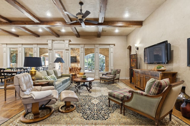 living room with arched walkways, ceiling fan, wood finished floors, baseboards, and beamed ceiling