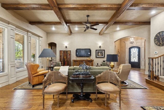 living room with arched walkways, coffered ceiling, beamed ceiling, hardwood / wood-style floors, and stairs