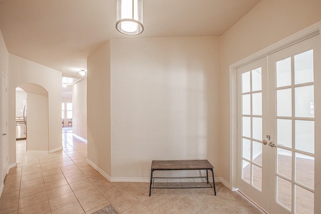 hallway featuring tile patterned floors, baseboards, arched walkways, and french doors