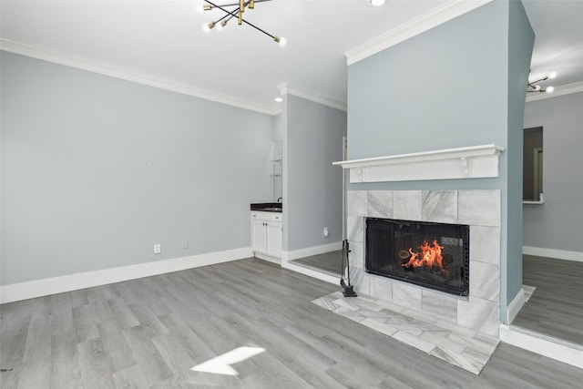 unfurnished living room featuring a notable chandelier, a tiled fireplace, crown molding, and light hardwood / wood-style floors