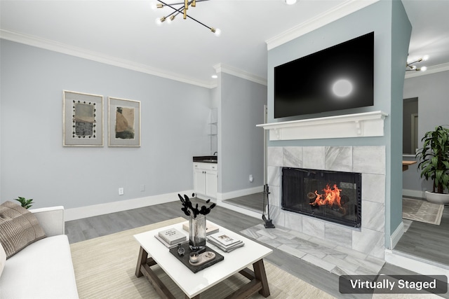 living room featuring ornamental molding, a tile fireplace, hardwood / wood-style floors, and a notable chandelier