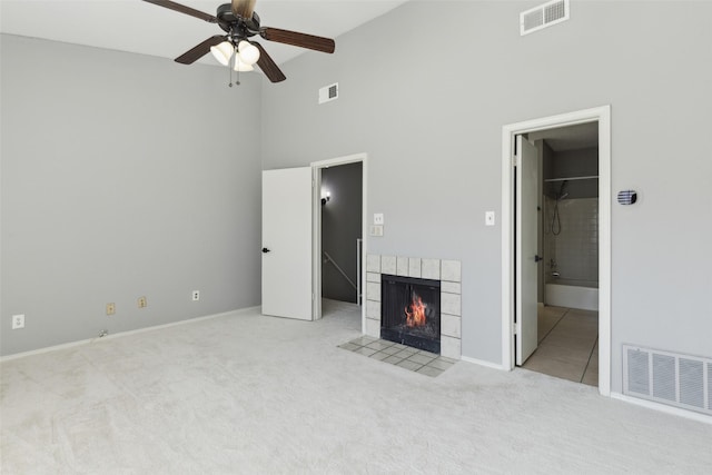 unfurnished living room featuring a tile fireplace, a towering ceiling, light colored carpet, and ceiling fan