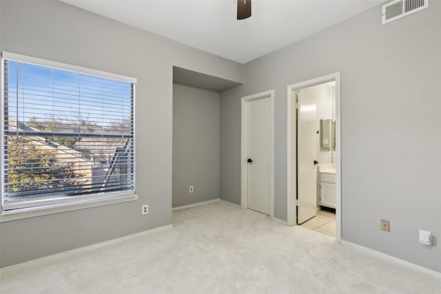 unfurnished bedroom with ceiling fan, ensuite bath, and light carpet