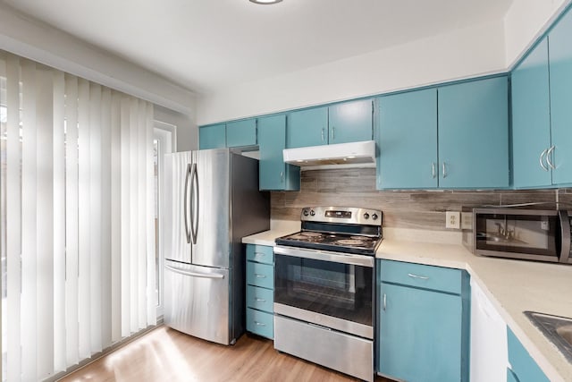 kitchen featuring decorative backsplash, blue cabinetry, stainless steel appliances, light countertops, and under cabinet range hood