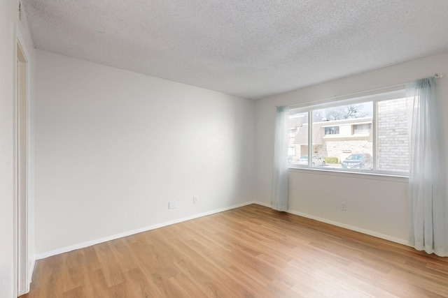 unfurnished room with light wood-style flooring, baseboards, and a textured ceiling