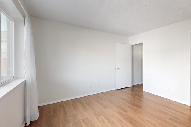 unfurnished room with light wood finished floors, baseboards, and a textured ceiling