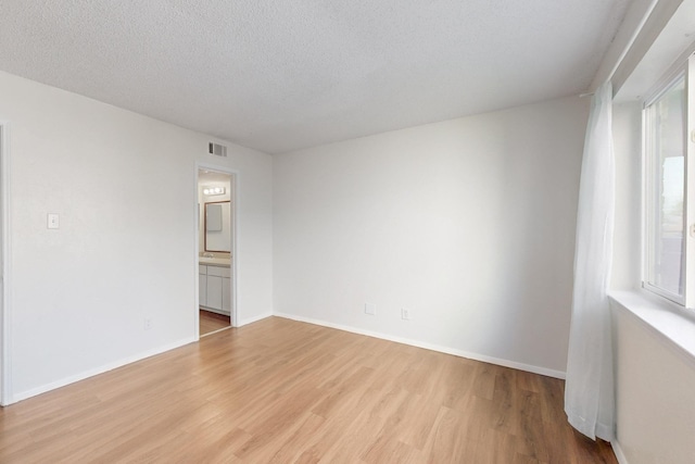 spare room with visible vents, light wood finished floors, a textured ceiling, and a wealth of natural light