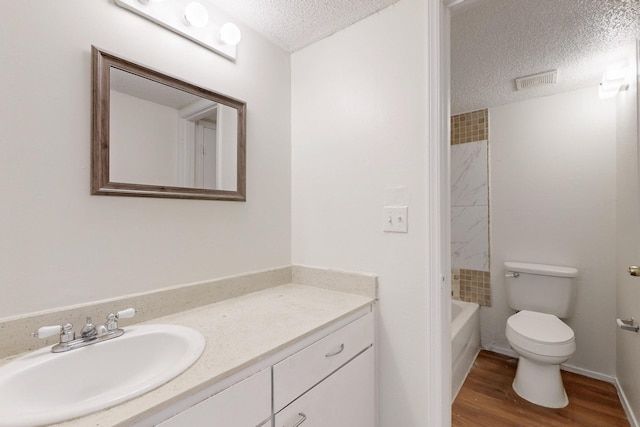 bathroom featuring a textured ceiling, bathtub / shower combination, toilet, wood finished floors, and vanity